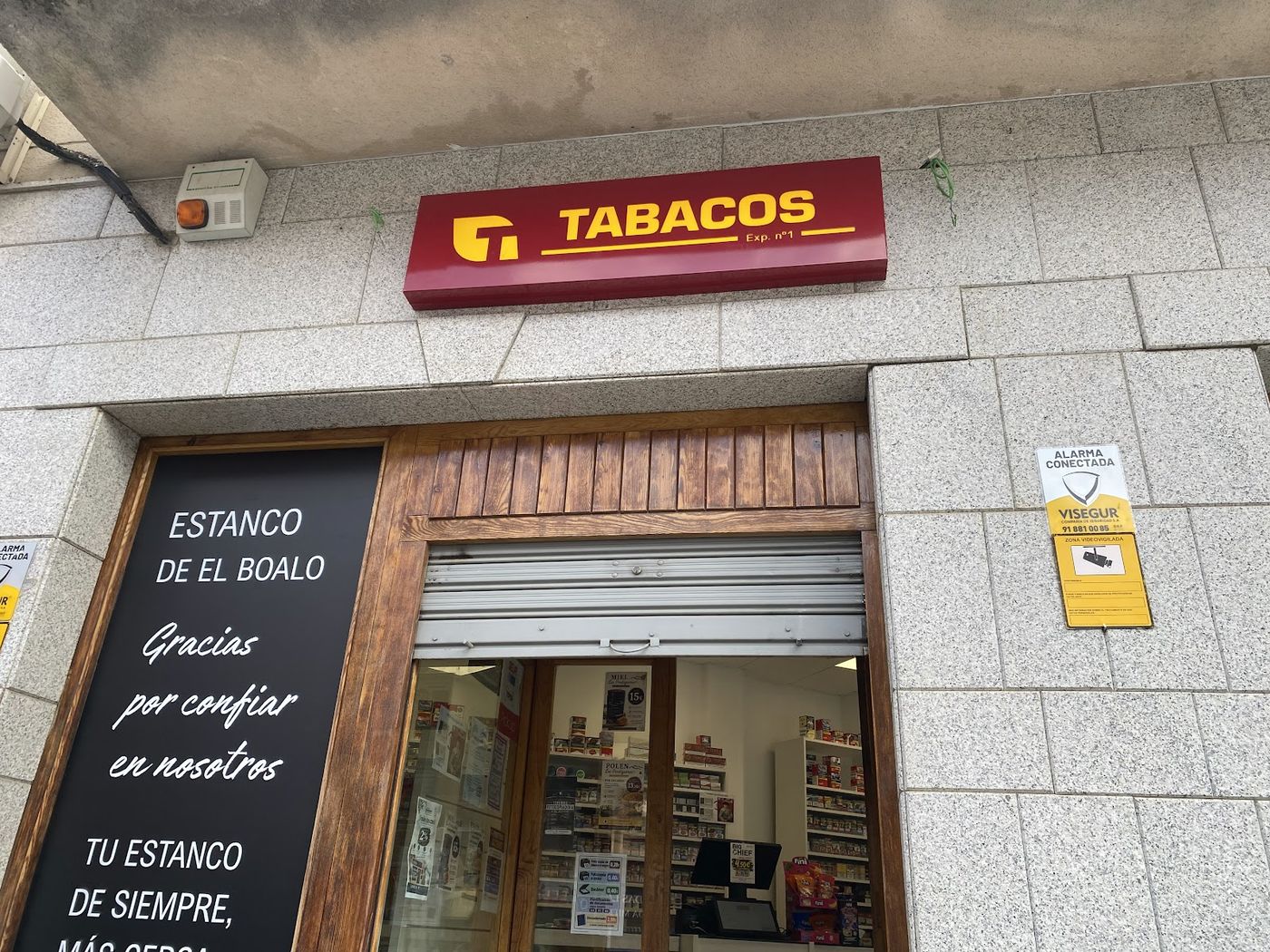 Fachada de granito del estanco con el rótulo rojo de Tabacos sobre la puerta