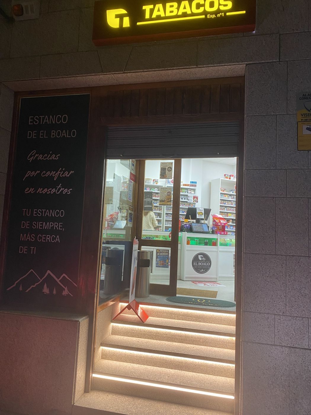 Entrada del Estanco El Boalo de noche, con el rótulo de Tabacos encendido y la escalera iluminada